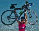Lynn West Salvo ’71 hoists her bike over her head on the beach